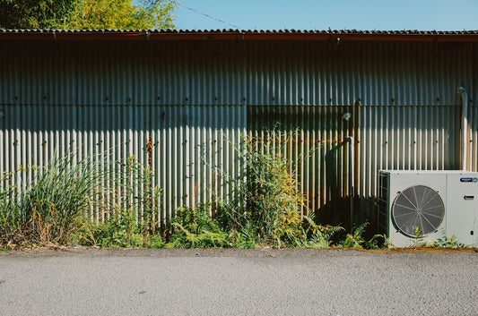 Corrugated metal wall with overgrown plants and air conditioner.