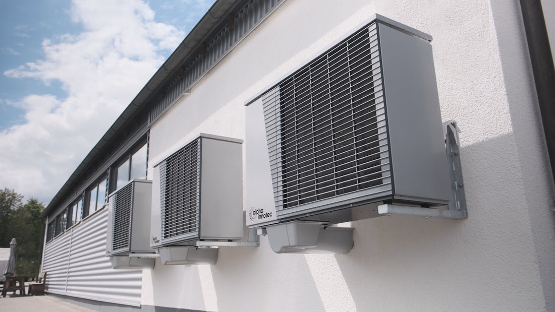 Three gray air conditioning units mounted on a white wall.
